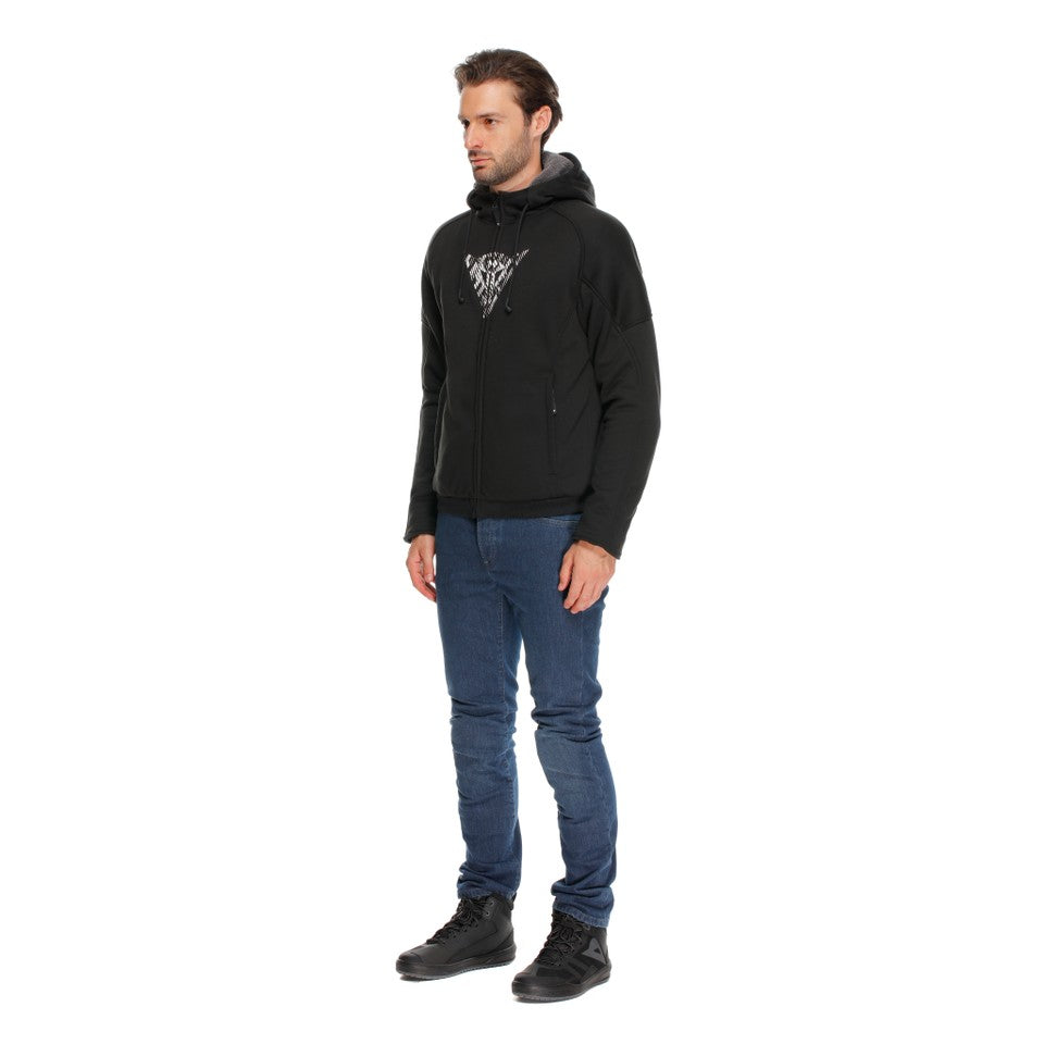 DAINESE BOVISA SAFETY HOODIE FULL ZIP 黑/白配色正面照，男性模特兒戴上連帽並拉起主拉鍊站立展示，胸前可見DAINESE白色三角品牌圖騰印花，內搭牛仔褲，義大利原廠刷毛連帽防摔衣，適合日常穿搭與換季騎乘
