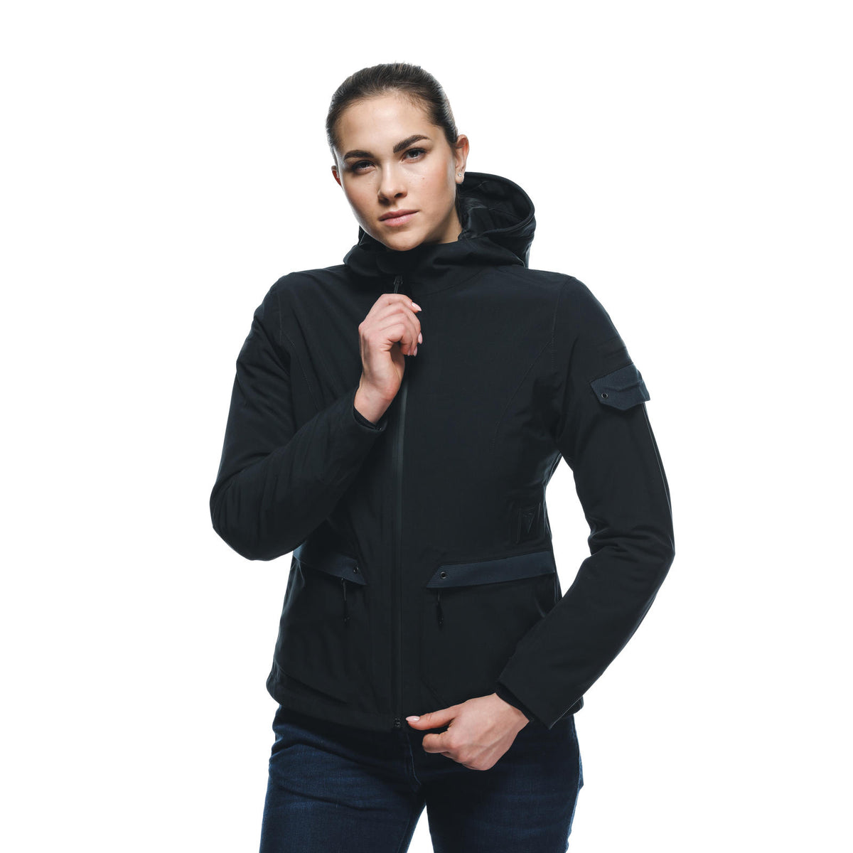 DAINESE CENTRALE ABSØLUTESHELL PRO JACKET WMN 黑色女模特兒正面全身照，連帽拉起雙手抓住領口拉鍊，可見臂部鬆緊帶口袋與中央拉鍊，黑色防水布料質感與修身剪裁