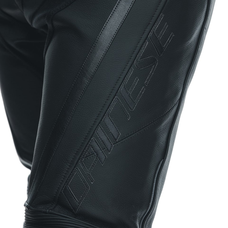 DAINESE DELTA 3 PERF.LEATHER PANTS 背面全身照，男性模特兒穿著打孔皮褲與車靴站立展示，可見腰際羅紋束帶、後臀立體剪裁與膝蓋RSS可替換式滑塊，義大利原廠Tutu小牛皮革局部打孔製賽道皮褲