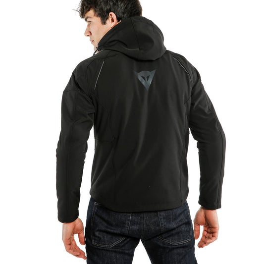 DAINESE IGNITE TEX JACKET 黑/黑配色背面照，男性模特兒戴上連帽站立展示外套背部剪裁，背部中央可見DAINESE三角品牌反光標誌與立體車縫線條，側邊口袋輪廓清晰，義大利原廠防風軟殼布料製都會防摔外套