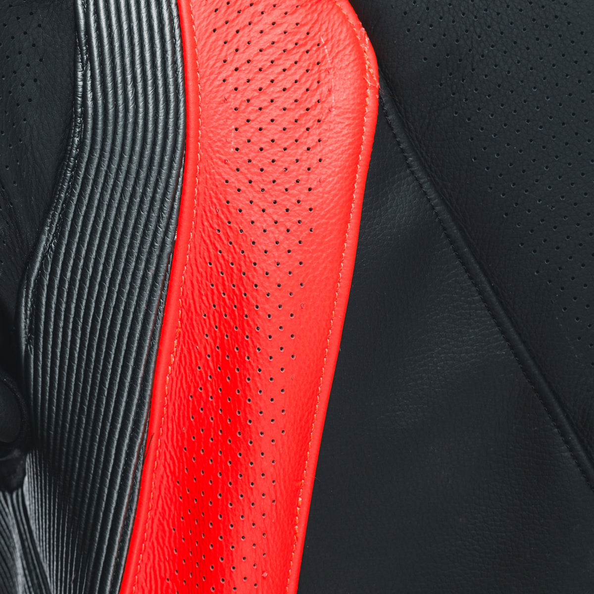 DAINESE AUDAX D-ZIP 1PC PERF. LEATHER SUIT 螢光紅打孔皮革細部特寫，可見透氣孔與車縫工藝
